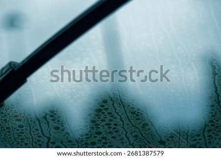 A car side window bears round marks from dried rain. Circles and rings overlap in a quiet pattern, the view of trees softened. The smooth pane catches light, a study of time and slow evaporation.