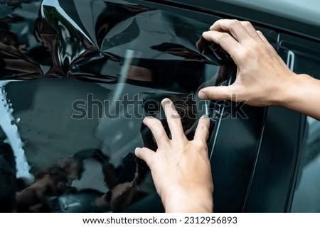 Car side window film removal and tinting installation. Male auto specialist worker hand gently carefully tinting the new protective car window film on glass surface.