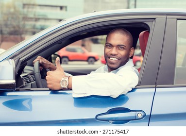 Car Side Window. Man Driver Happy Smiling Showing Thumbs Up Driving Sport Blue Car Isolated Outside Parking Lot Background. Handsome Young Man Excited About His New Vehicle. Positive Face Expression