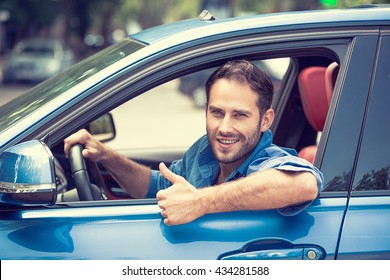 Car Side Window. Man Driver Happy Smiling Showing Thumbs Up Driving Sport Blue Car Isolated Outside Parking Lot Background. Handsome Young Man Excited About His New Vehicle. Positive Face Expression