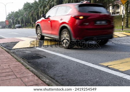 Car slowing down at speed bump or road hump painted in yellow and black stripe. Motion blur intended.