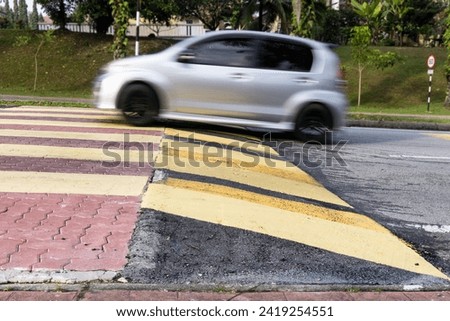 Car slowing down at speed bump or road hump painted in yellow and black stripe. Motion blur intended.