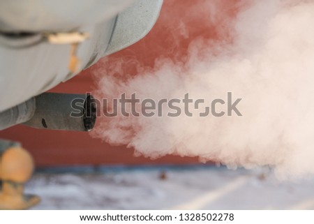 The car smokes in the winter. Smoke from a car pipe. The car is buzzing in the cold. The car is buzzing in the winter outside.