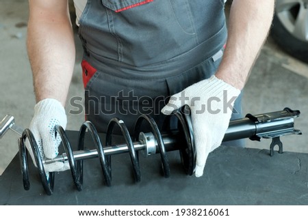 Car spare parts. Shock absorber strut and spring in the hands of a mechanic, close-up. Inspection of the compatibility of the spring part and the shock absorber strut.
