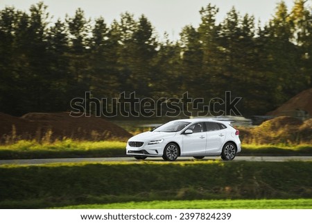 Car speeding in the countryside. Driving fast on a road surrounded by greenery in a modern hatchback. Side view of modern hatchback moving on the highway.