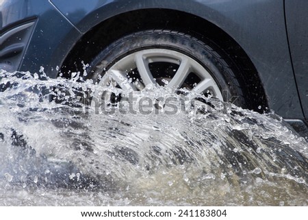 Car splashes through a large puddle on a flooded street 