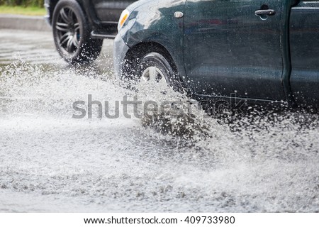 Car splashes through a large puddle on a flooded street 