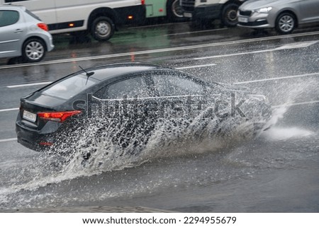 Car splashing water, driving through puddle at heavy rain. Car driving on flooded asphalt road at heavy rain, wet road. Dangerous driving conditions, risk of aquaplaning. MOTION BLUR.