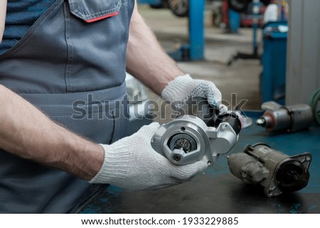 The car starter is new in the hands of a mechanic. Next to it, on the desktop, is a faulty starter. Inspection of the spare part before installation. Car repair and maintenance.