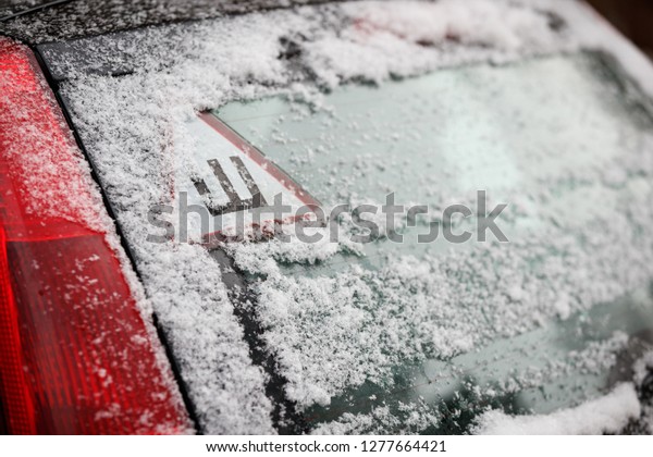 Car sticker with a Russian letter denoting spikes\
on a car\'s snow-covered rear window. The sign warns drivers that\
the car is equipped with spiked wheels. Safe movement on icy roads\
in winter