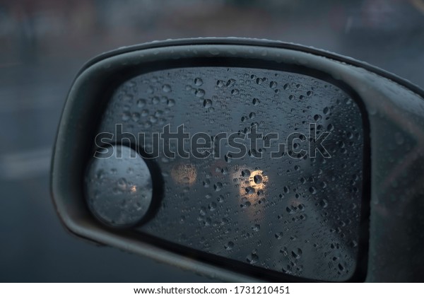 Car stop amid heavy rain on street with view\
of moving bokeh light in rear view mirror. Rain drops on side car\
mirror as cars moving pass. Bokeh on rear view mirror & car\
moving amid rain concept.  
