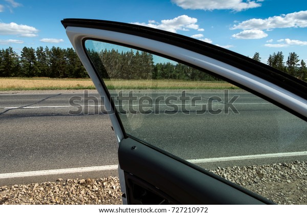 Car stop on the\
roadside.\
Horizontally. Toning. The open door of the car stopped\
at the side of the highway. The sun shines through the tinted\
glass, clouds.