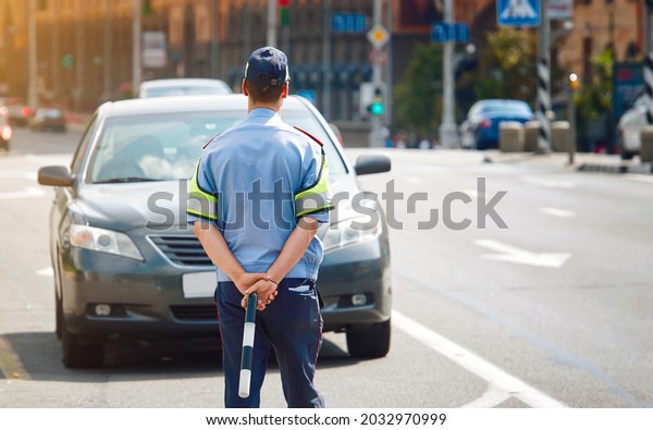 Car stopped by traffic police officer to check\
driver\'s license and automobile registration. Police officer stops\
car at roadside. Officer with police stick on duty, prevent moving\
violations