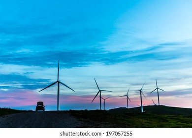 Car stopping by the side of the road together with wind turbines standing on the hill against the dusk twilight blue sky