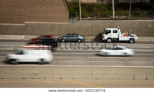 Car
stranded on shoulder of freeway with tow truck stopped behind it
and traffic blurred as cars speed by the
scene