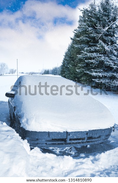 Car stuck and covered in thick\
snow after Winter snow storm blizzard covered entered\
landscape.