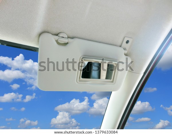 Car sun visor and mirror in car with sky and\
clouds as a backdrop.