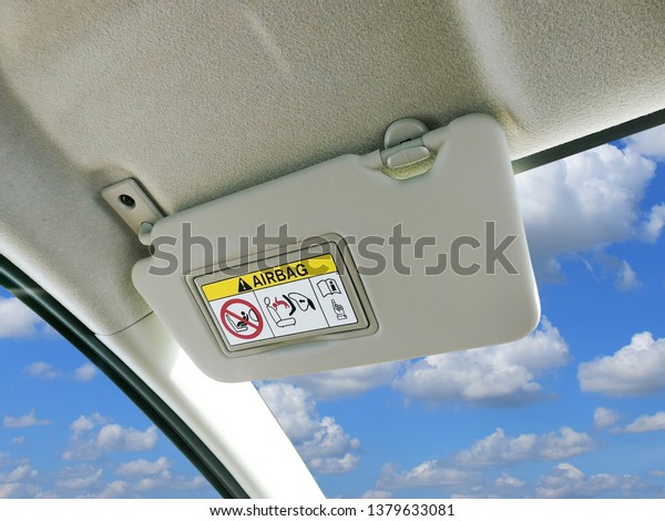 Car sun visor and warning signs of\
airbag system in car with sky and clouds as a\
backdrop.