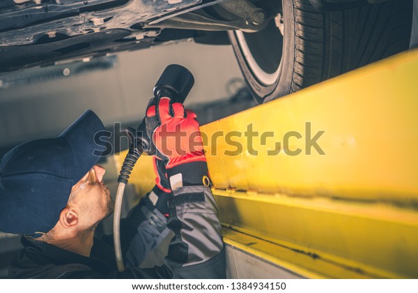 Car Suspension\
Issue. Caucasian Auto Mechanic with Flashlight Looking For\
Potential Problem Under the\
Vehicle.