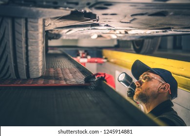 Car Suspension Issue. Caucasian Vehicle Mechanic With Flashlight Inspecting Car Undercarriage.