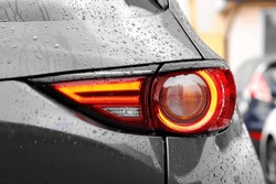 Car With Switched On Tail Light In Drops Of Water Outdoors, Closeup