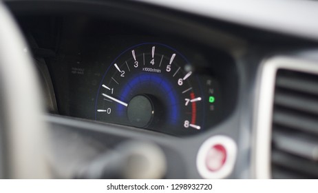 Car tachometer with a blurry dashboard and steering wheel