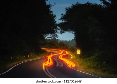 Car Tail Light Trails On A Winding Road At Night In Forest.