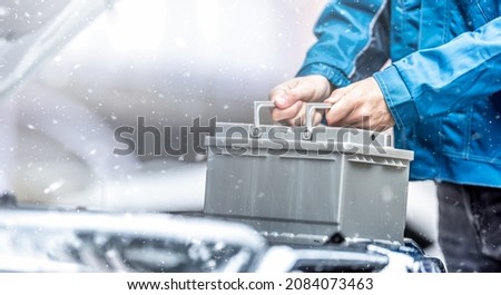 Car technician replaces dead car battery in winter conditions. 