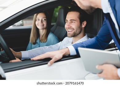Car test-drive concept. Caucasian young family testing trying new car before buying purchasing it while male shop assistant helping them to choose with digital tablet. - Powered by Shutterstock