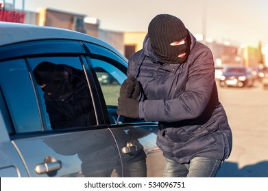 Car Theft, Male Thief In Black Robbery Mask Breaking Into Car Using Screwdriver.