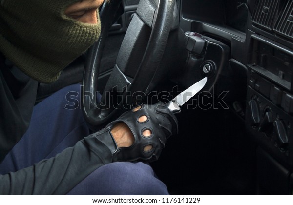 Car theft in mask and black gloves\
breaking down the car lock. Carjacking\
concept