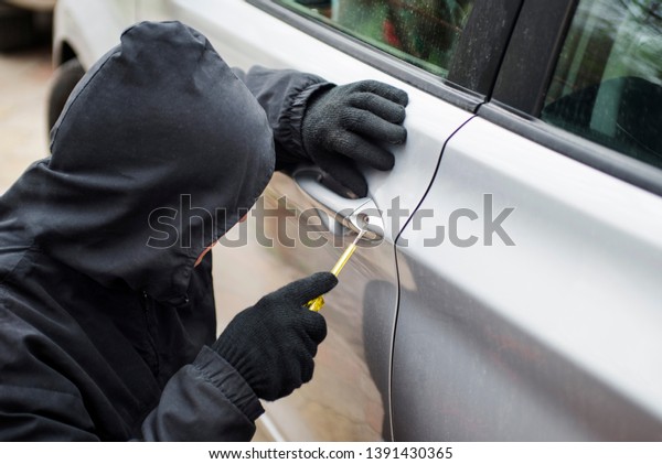 Car thief in action.\
Thief stealing automobile car. The man dressed in black trying to\
break into the car.