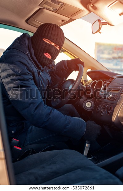 Car thief in\
black balaclava stealing\
auto.