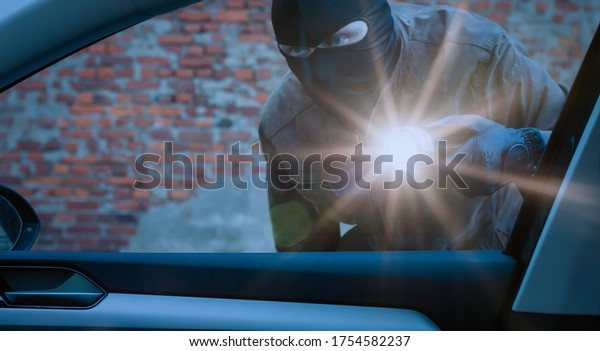 car thief\
examines a car with a flashlight at\
night