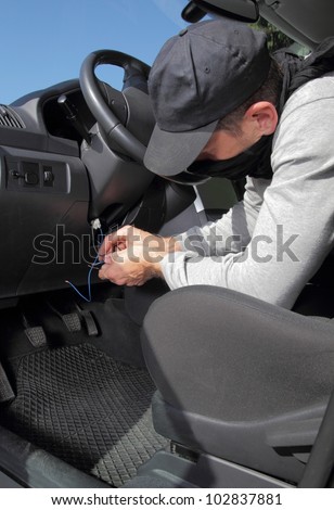 Car thief hot wiring the electrical circuits on the ignition of a car as he prepares to steal it