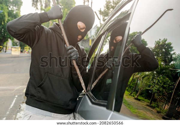 Car thief man with a tool trying to break window\
car on the street