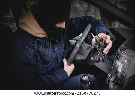 A car thief in a mask excluding recognition, tries to open the ignition lock with a tool. Crime, car theft