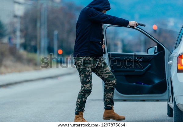 The car thief is pulling the car owner out of his
car and trying to get the car while pointing a loaded gun at the
drivers head.