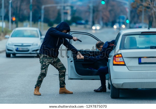 The car thief is pulling the car owner out of his\
car and trying to get the car while pointing a loaded gun at the\
drivers head.