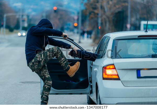 The car thief is pulling the car owner out of his\
car and trying to get the car while pointing a loaded gun at the\
drivers head.