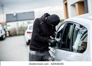 Car thief trying to break into a car with a screwdriver. Car thief, car theft.