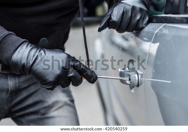 Car thief trying to break into a car with a
screwdriver. Car thief, car
theft.