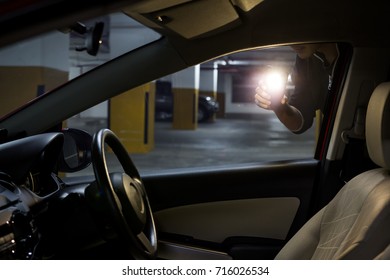 Car thief using flashlight look inside a car in a parking lot. Car robbery concept.