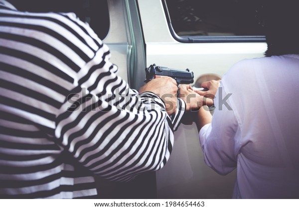Car thieves hold a gun to rob a car from a woman\
who owns it. Close-up photo. Insurance concept. Protection of life\
and property