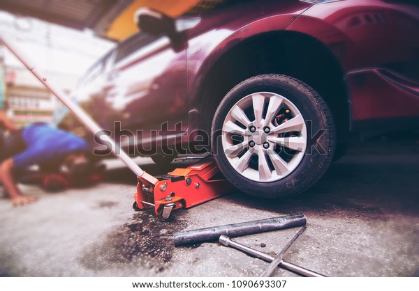 Car tire changed for maintenance in\
garage using hydraulic jack - car maintenance\
concept