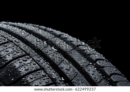 Car tire covered with water drops on black background