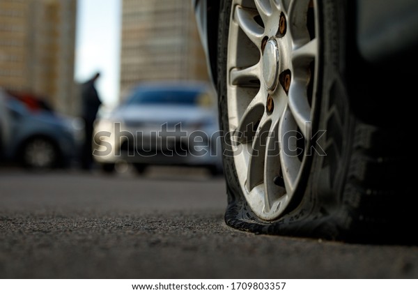 Car tire with a flat
tire in the yard near a multi-storey building. Image of an
accident, damage, breakdown for illustration on the topic of
repair, insurance. Blurred