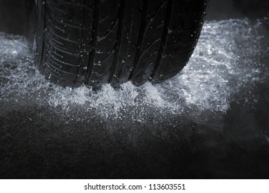 A Car Tire On A Wet Road. The Rain Groove Is A Design Element Of The Tread Pattern Specifically Arranged To Channel Water Away From The Footprint.