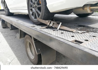 Car tire secured with belt for safety on flatbed tow truck