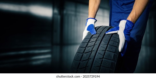car tire shop and service - mechanic holding new tyre on garage background. copy space 